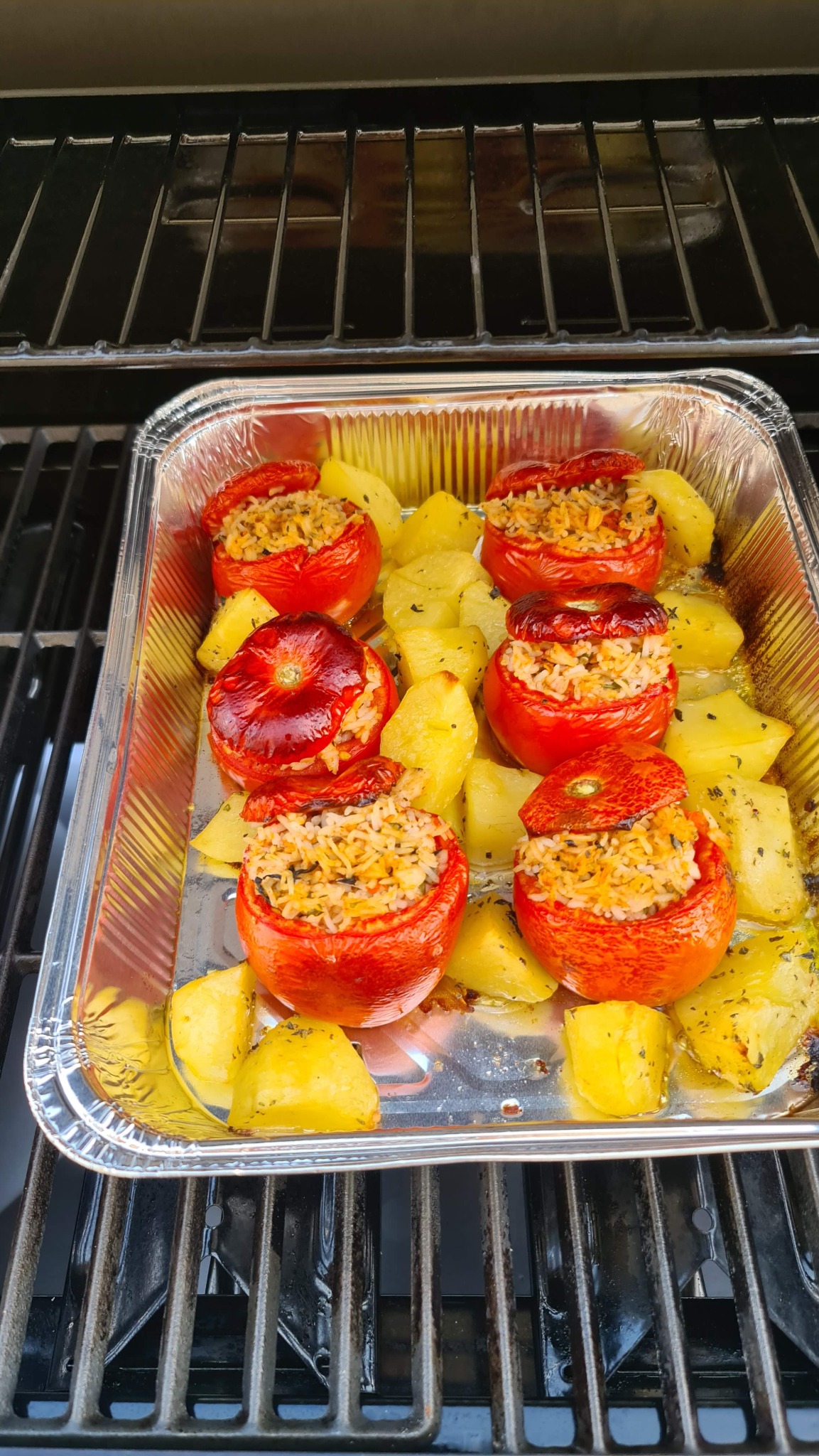 Vaschetta nel barbecue con i pomodori ripieni e le patate già cotti